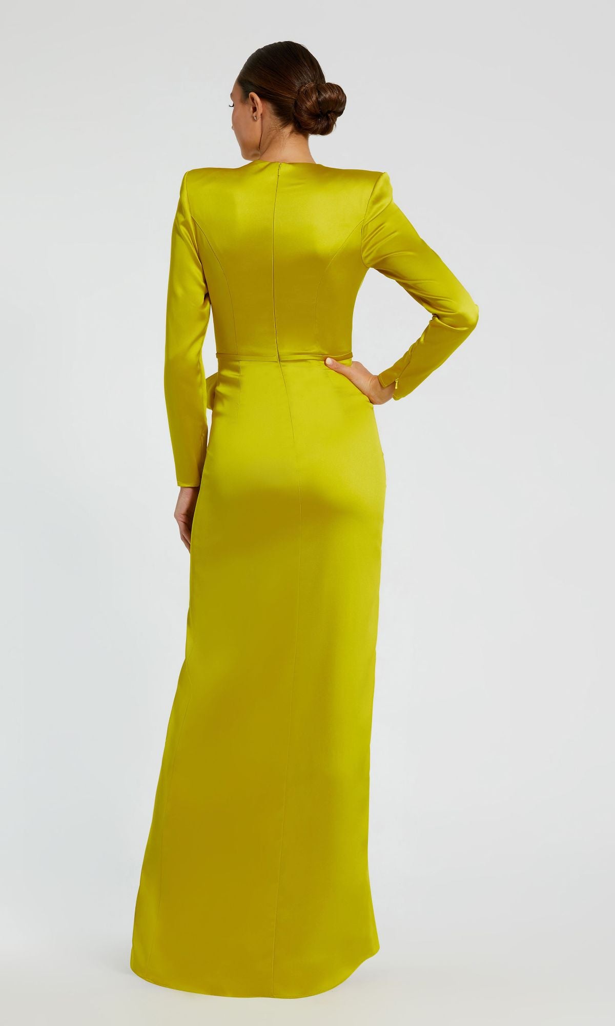 A person stands facing away, wearing the Mac Duggal 26676 Bold-Shoulder Long Formal Dress in yellow-green, featuring a bra-friendly fitted silhouette, high neckline, and floor-length elegance.
